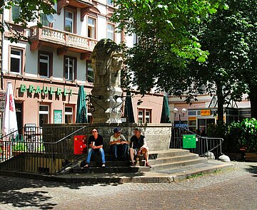 Drei Männer sitzen auf den Stufen des Indianerbrunnes auf dem Werderplatz.