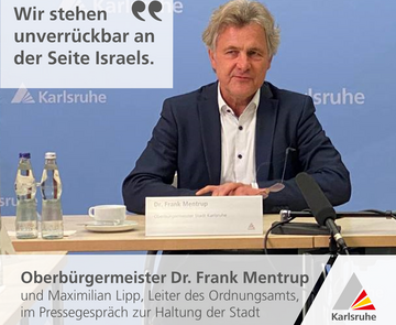 Oberbürgermeister Dr. Frank Mentrup sitzt vor einer blauen Pressewand der Stadt Karlsruhe.