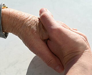 Eine Hand eines jungen Menschen hält die Hand einer älteren Person.