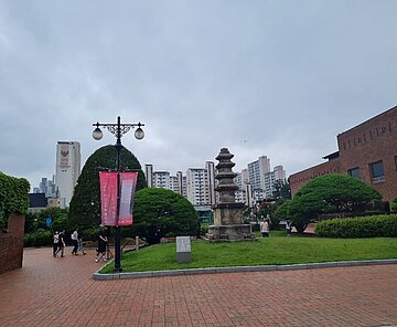 Parkähnlicher Platz mit Menschen, im Hintergrund Hochhäuser
