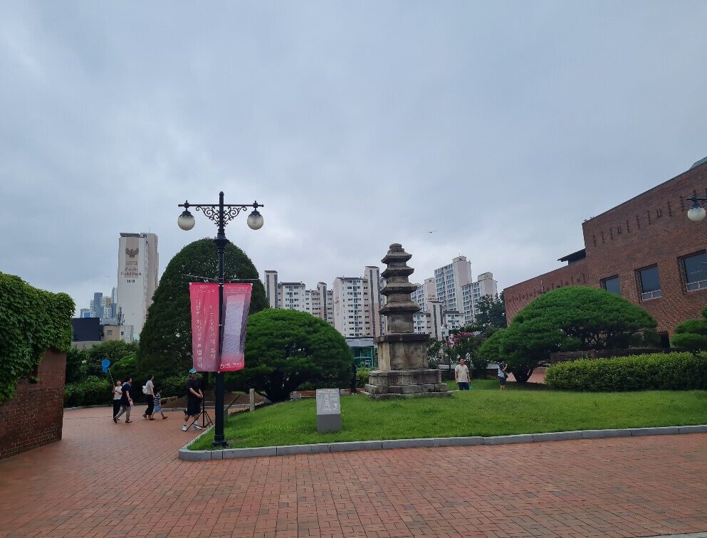 Parkähnlicher Platz mit Menschen, im Hintergrund Hochhäuser