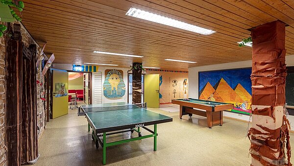 Zu sehen ist der Flurbereich im Keller mit einer alten Holzdecke und Linoleumboden, ausgestattet mit einer Tischtennisplatte und einem Billardtisch. Das Einrichtungsmotto dieser Zeit war Ägypten.