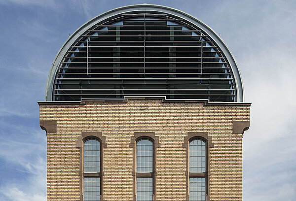 Nahaufnahme der westlichen Giebelseite des Tonnendachs mit Fensterband, die restlichen Teilflächen sind aus geschlossenen Paneelen.