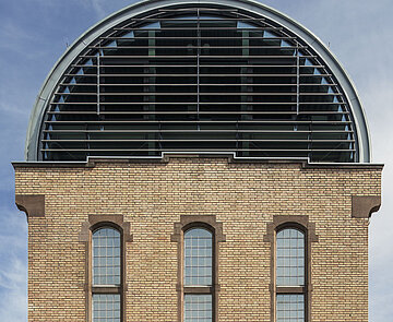 Nahaufnahme der westlichen Giebelseite des Tonnendachs mit Fensterband, die restlichen Teilflächen sind aus geschlossenen Paneelen.