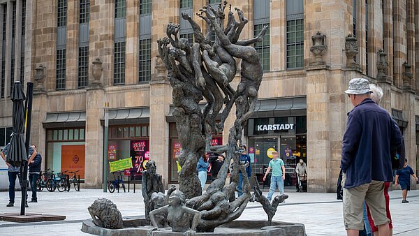 Zwei Passanten betrachten den Lammbrunnen in der Innenstadt vorm Karstadtgebäude
