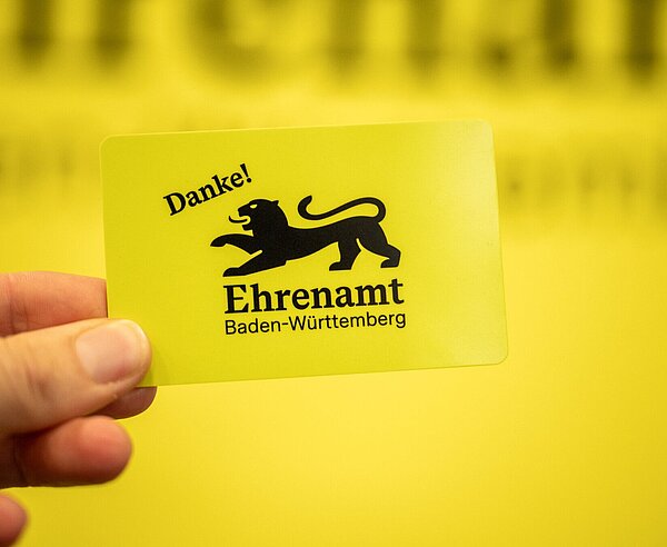 Hand hält gelbe Ehrenamtskarte Baden-Württemberg 