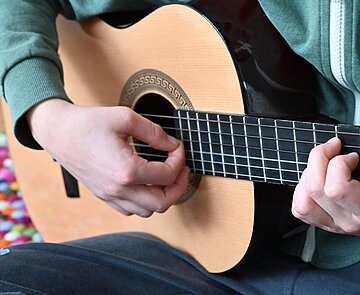 Kind spielt sitzend auf dem Boden Gitarre.