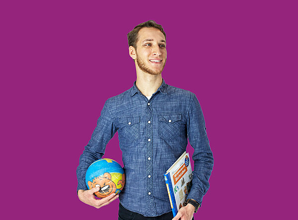 Mann mit Ball und Buch in den Händen vor lila Hintergrund