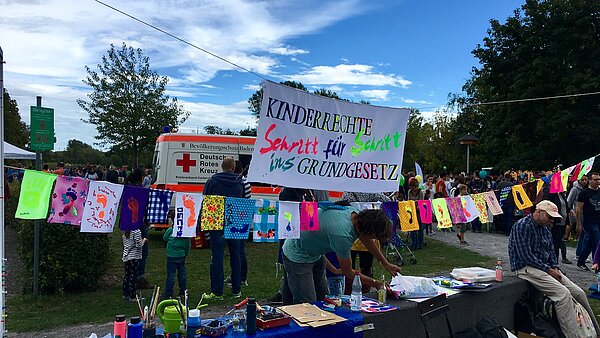 Aufgehängte bunte Plakate, davor Tische und Menschen.