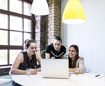 Drei Studentinnen arbeiten im Team an einem Laptop.