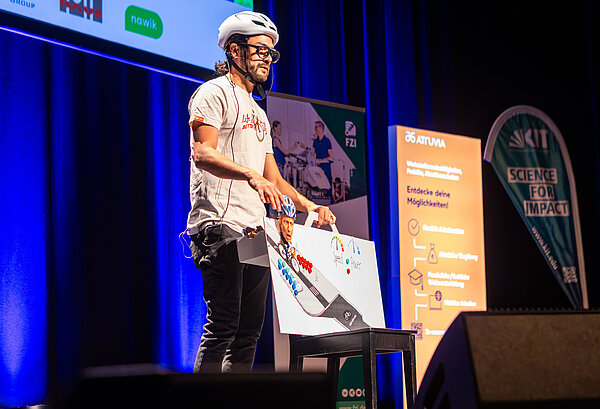 Ein FameLab-Kandidat hält seinen Vortrag über Radverkehr mit einem Fahrradhelm auf.