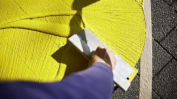 Jemand spachtelt gelbe Farbe auf den Boden im Passagehof