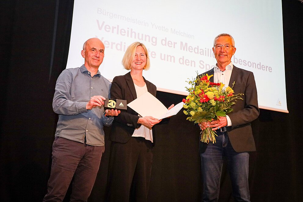Die Medaille für besondere Verdienste um den Sport erhielt der ehemalige Sportbürgermeister Dr. Martin Lenz  (r.), überreicht vom Vorsitzenden des Sportkreises Dr. Andreas Ramin (l.) und Bürgermeisterin Yvette Melchien.