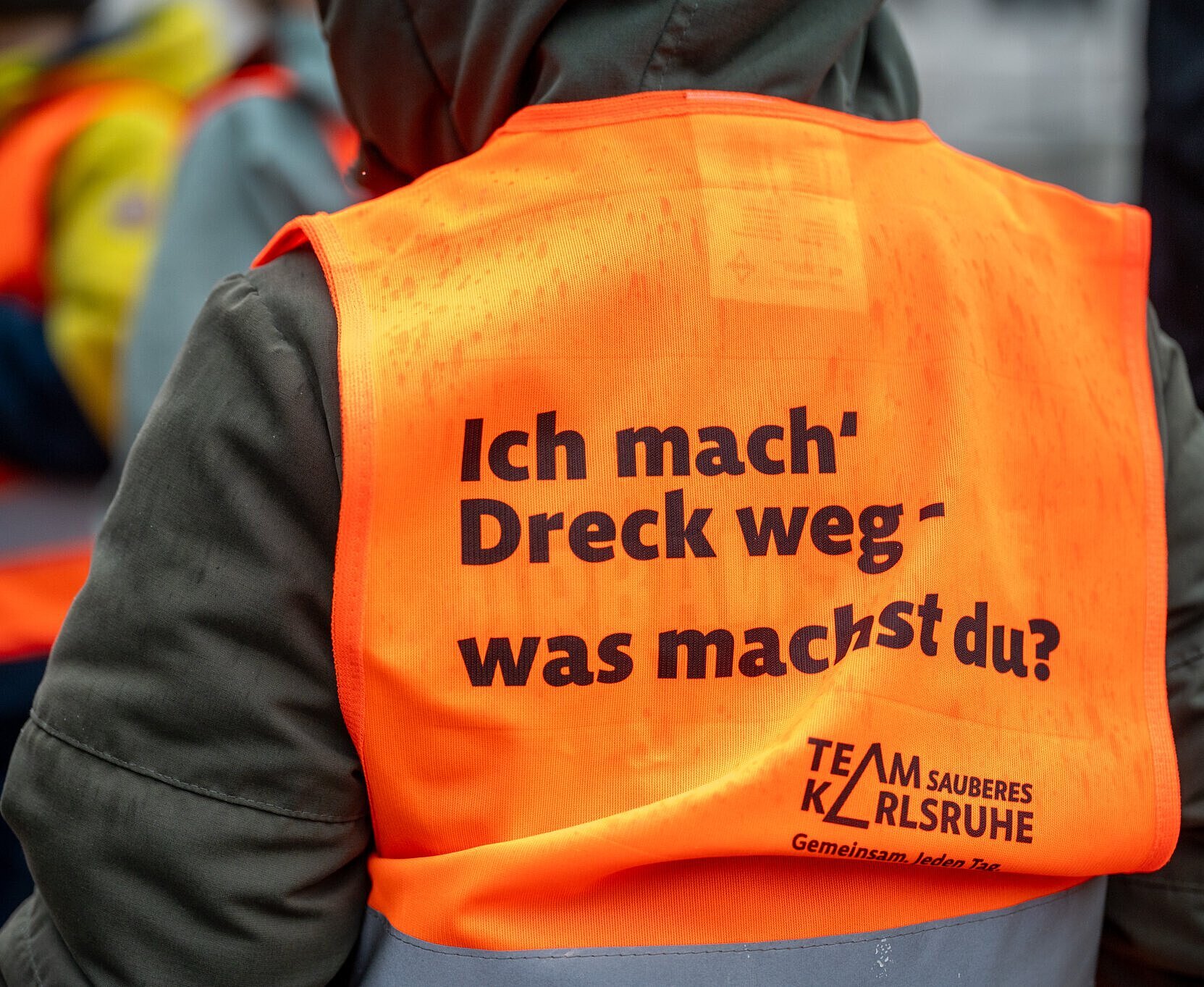Kindergartenkinder in Warnweste "Ich mach Dreck weg" von hinten fotografiert