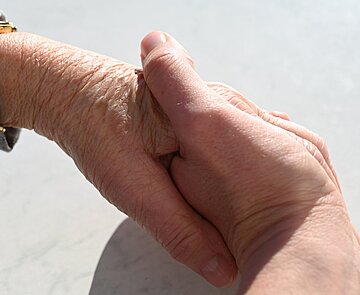 Eine Hand eines jungen Menschen hält die Hand einer älteren Person.