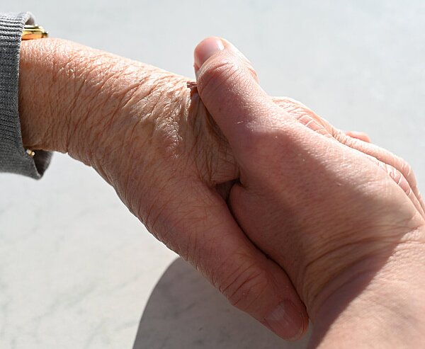 Eine Hand eines jungen Menschen hält die Hand einer älteren Person.