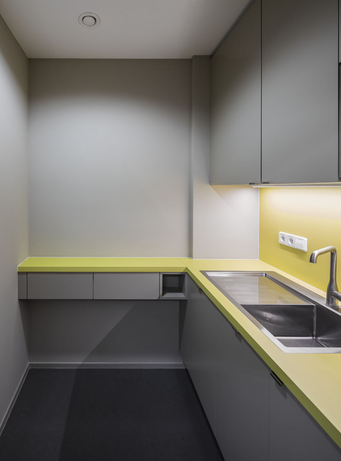 Blick auf die Teeküche mit auffälligen grünen Akzenten und einem Edelstahl-Waschbecken.