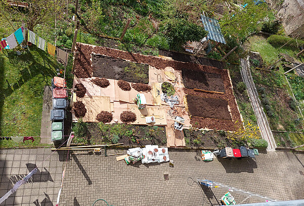 Vogelperspektive auf Gartenbeete im Frühjahr, die frisch angelegt sind und mit Karton und Rindenmulch umrandet sind.
