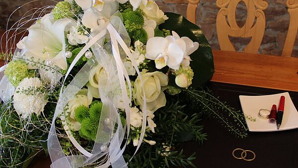 Tisch mit Blumenbouquet, Trauringen und Tintenfüller.