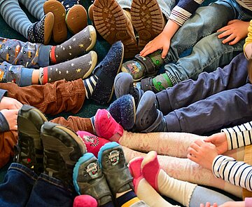 Kinder sitzen im Kreis auf dem Boden und strecken ihre Beine in die Mitte.