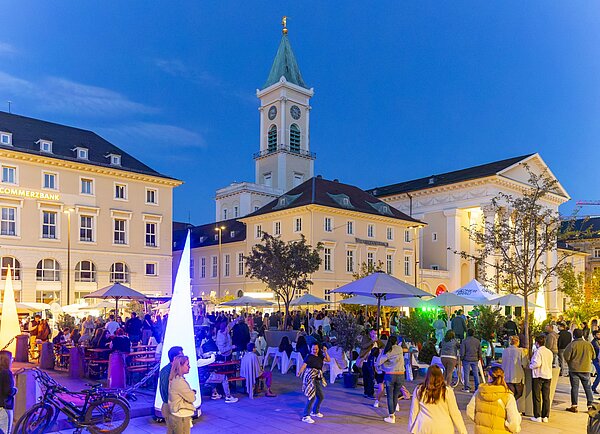 Marktplatz Karlsruhe mit Blick auf die Pyramide mit einer Menschenmenge bei der Veranstaltung „Lounge 76“.  Im Hintergrund ist die evangelische Stadtkirche zu sehen.