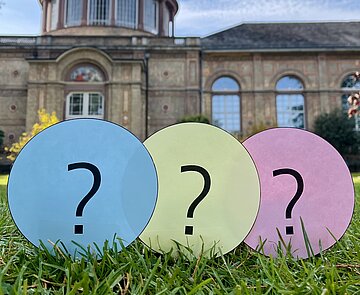 Fragezeichen auf runden Karten auf einer Wiese.