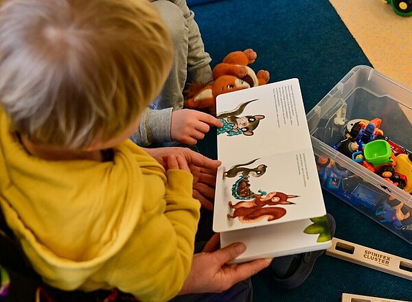 Eine Erzieherin liest mit zwei Kindern ein Buch.