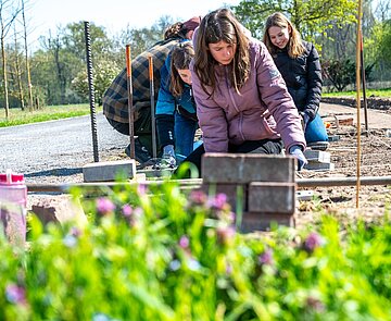 Hier stellten drei Schülerinnen auf Knieschonern eine Mähkante her – die Abgrenzung einer Rasenfläche – indem sie Pflastersteine in den Boden einbringen, ausgerichtet an einer Schnur. 