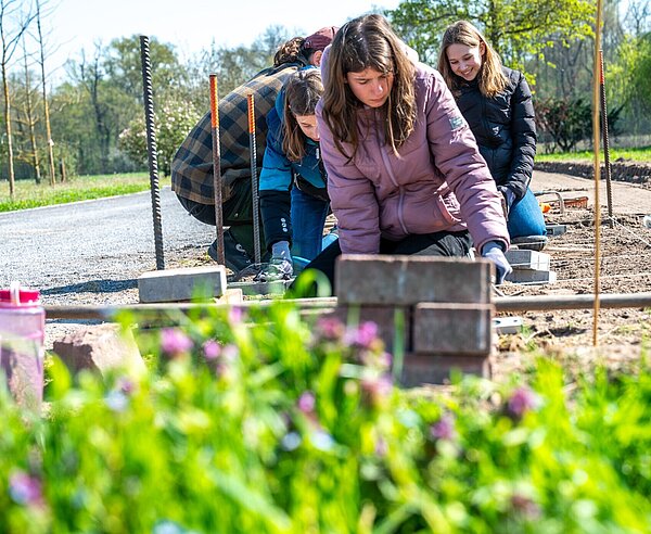 Hier stellten drei Schülerinnen auf Knieschonern eine Mähkante her – die Abgrenzung einer Rasenfläche – indem sie Pflastersteine in den Boden einbringen, ausgerichtet an einer Schnur. 