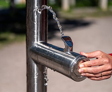 Eine Hand bedient den Trinkbrunnen und frisches Wasser sprudelt 