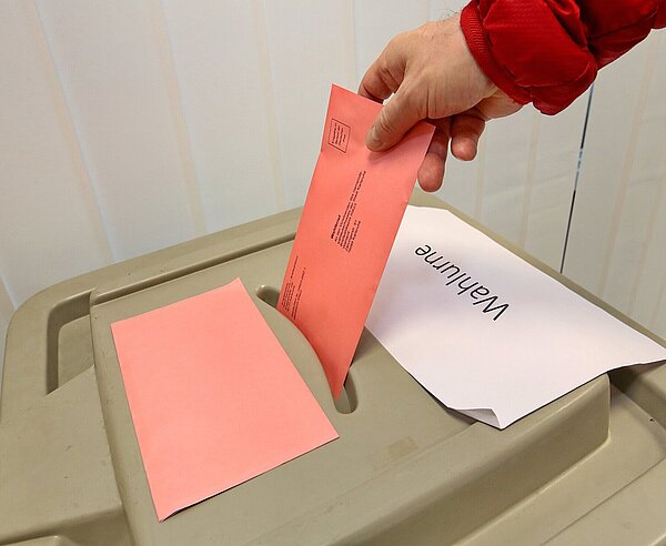 Roter Wahlbrief wird in Wahlurne geworfen