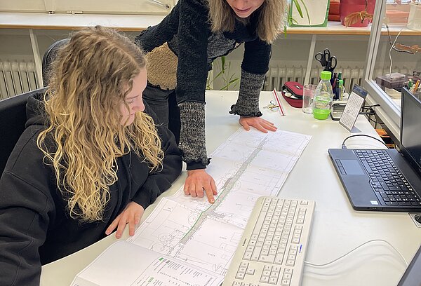 Junge Frau mit Ausbilderin mit Plänen