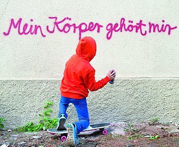 Kind kniet vor einer Mauer mit Spraydose in der Hand. An der Mauer steht „Mein Körper gehört mir“.