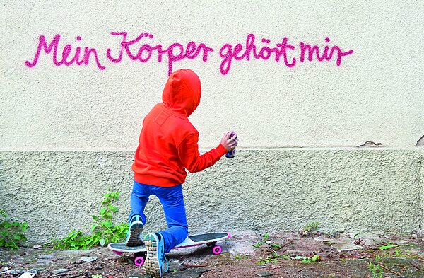 Kind kniet vor einer Mauer mit Spraydose in der Hand. An der Mauer steht „Mein Körper gehört mir“.