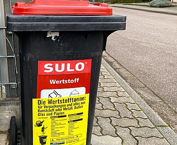 Wertstofftonne mit Gurdulic Aufkleber steht am Straßenrand