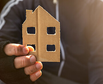 Obdachloser hält ein Haus aus Pappe in der Hand