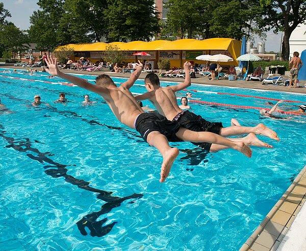 Zwei Jungen springen in ein Schwimbecken