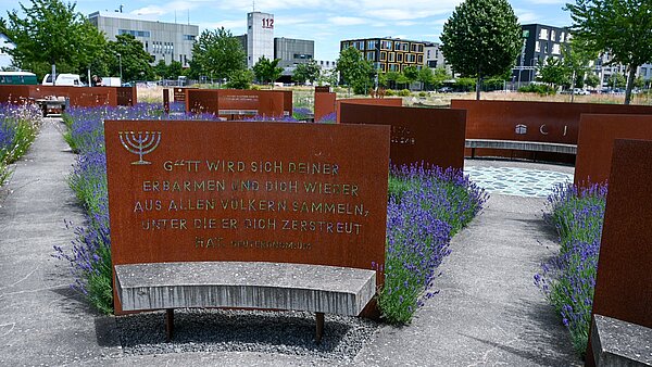 Impression aus dem Garten der Religionen Sitzbank mit jüdischem Leuchter Menora und Zitat aus dem Deuteronomium