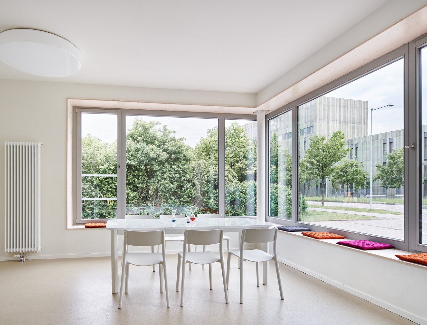 Zu sehen ist ein Büroraum mit einer Tischgruppe in der Mitte, Kautschukboden und einem Eckfenster mit Fensterbänken zum Sitzen.