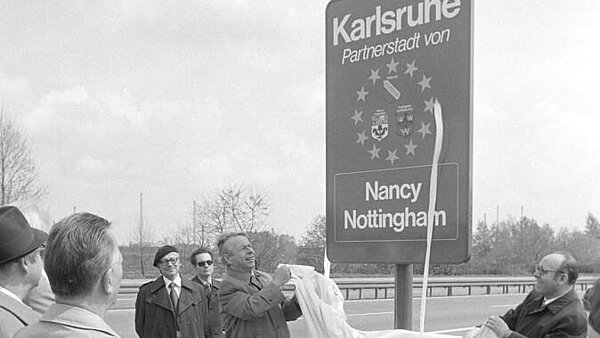 Oberbürgermeister Otto Dullenkopf (links) und der 1. Vorsitzende des Freundeskreises Gustav Betz bei Enthüllung der Tafel an einer Ortseinfahrt von Karlsruhe. Dabei Zuschauende.