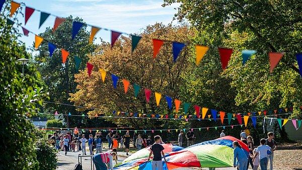 Mehrere Kinder spielen mit einem Schwungtuch im Rahmen der Aktion Karlsruhe spielt! 2026 in mit Wimpelketten geschmückter Straße in der Waldstadt