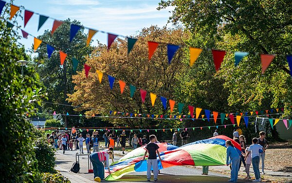 Mehrere Kinder spielen mit einem Schwungtuch im Rahmen der Aktion Karlsruhe spielt! 2026 in mit Wimpelketten geschmückter Straße in der Waldstadt