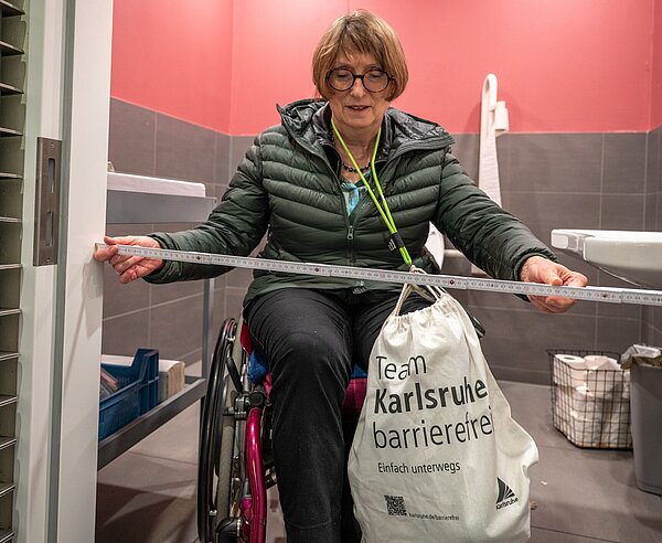Die Türbreite einer Behindertentoilette in der Eismanufaktur Claus wird von einer Rollstuhlfahrerin vermessen.