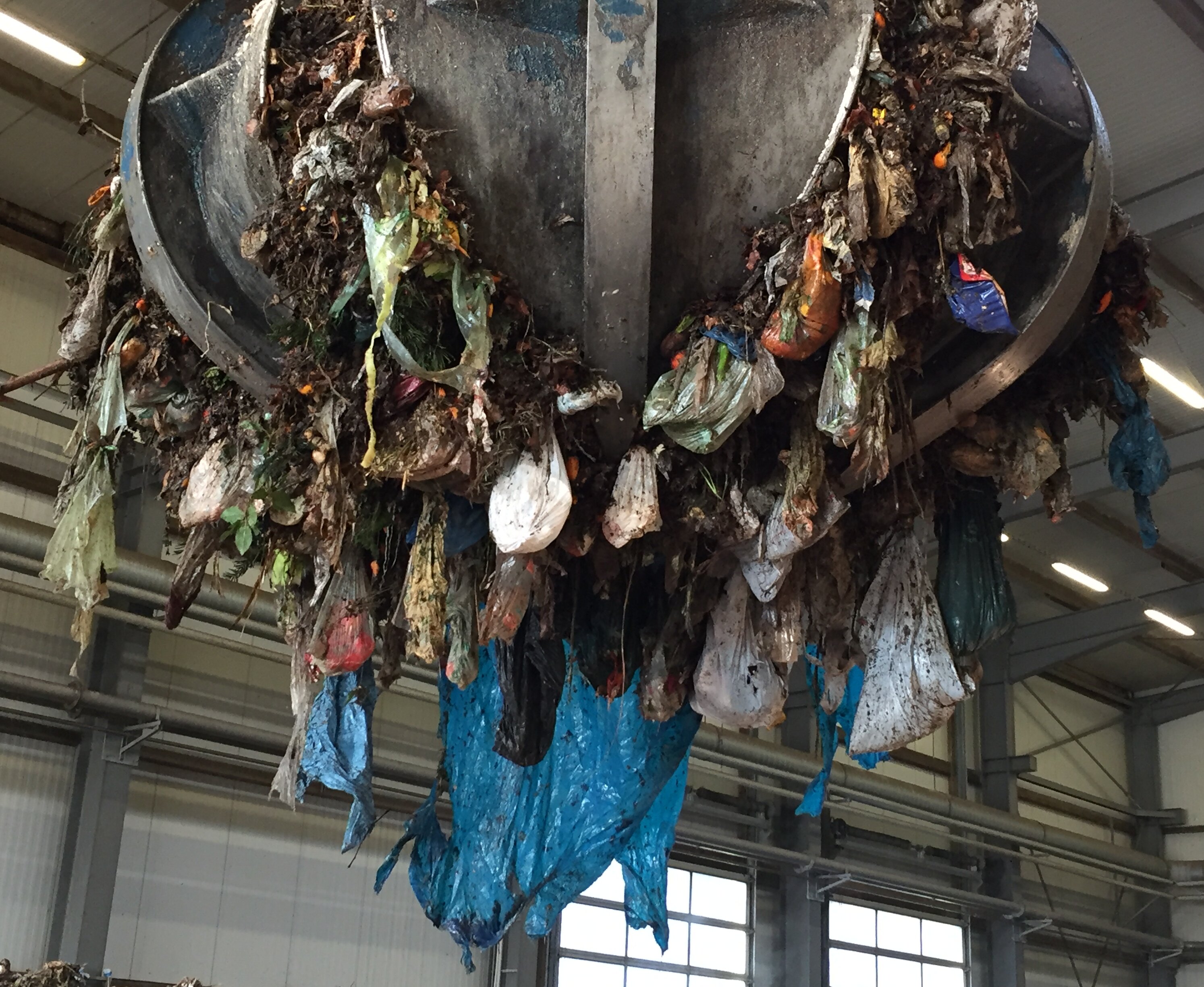 Ein Greifarm hebt Biomüll an. Dabei sind viele Plastiktüten zu sehen.