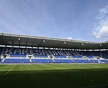 Ansicht des leeren Spielrasens. Die leeren Sitzplätze ergeben "Karlsruher SC".