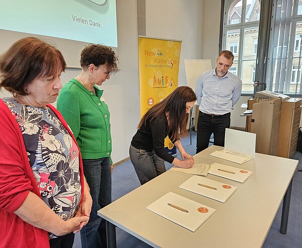 Meri Uhlig, Integrationsbeauftragte der Stadt Karlsruhe, unterzeichnet die Kooperationsvereinbarung vor den Partnerorganisationen von AniKA während des vergangenen Bündnistreffens .