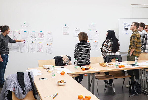 Person präsentiert Entwürfe an der Wand vor Gruppe von Zuschauern