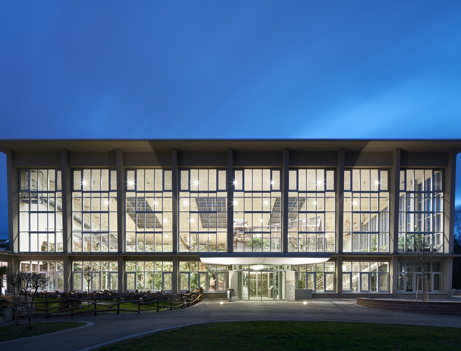 Blick auf die glasreiche, beleuchtete Westfassade des Exotenhauses bei Dämmerung.