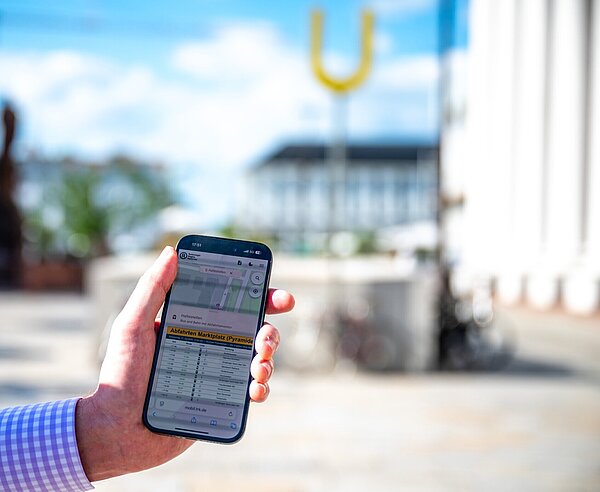 Handy mit Mobilitätsapp informiert über Abfahrtszeiten vom Marktplatz/Pyramide