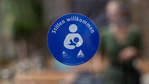 Ein Aufkleber mit der Aufschrift "Stillen Willkommen" an einer Glasscheibe
